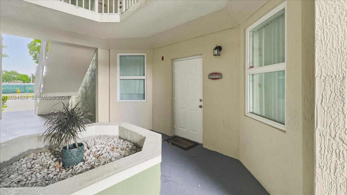 A white door with a small plaque sits on a covered walkway near a planter — 11102 NW 83rd St # 108, Doral FL 33178, DORAL, FL