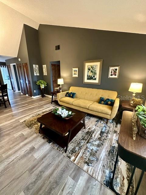 A living room features a yellow sofa, a dark wood coffee table, and wood-look flooring — 4833 MYRTLE OAK DRIVE UNIT 25, NEW PORT RICHEY, FL