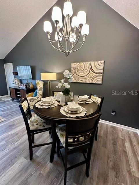 A dining area features a round wooden table, four chairs, and a chandelier under a vaulted ceiling — 4833 MYRTLE OAK DRIVE UNIT 25, NEW PORT RICHEY, FL