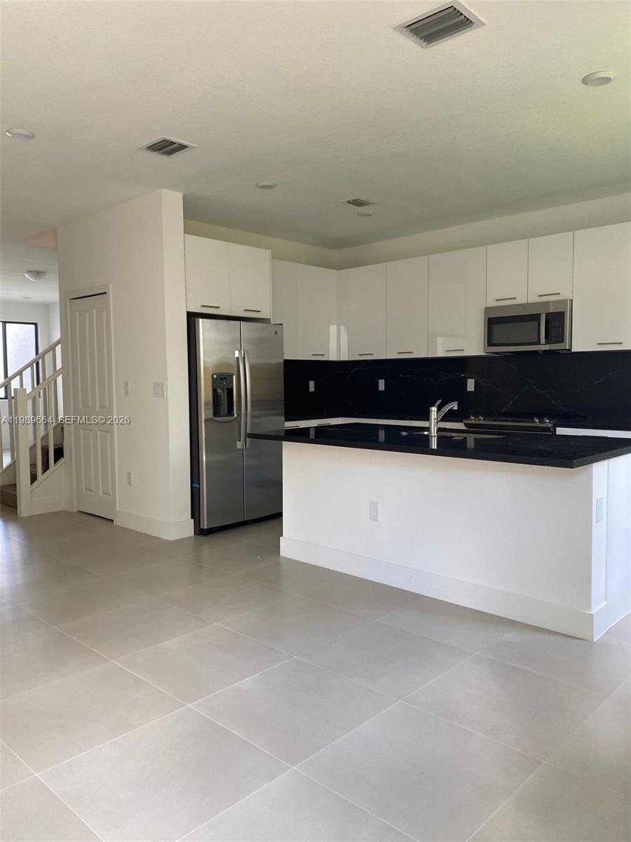 A modern kitchen features white cabinets, black countertops, stainless steel appliances, and light tile flooring — 13633 SW 157th Pl # 0, Miami FL 33196, MIAMI, FL