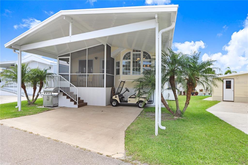 A manufactured home with a large carport, screened porch, and a golf cart parked underneath — 3333 26TH AVENUE E UNIT 1104, BRADENTON, FL