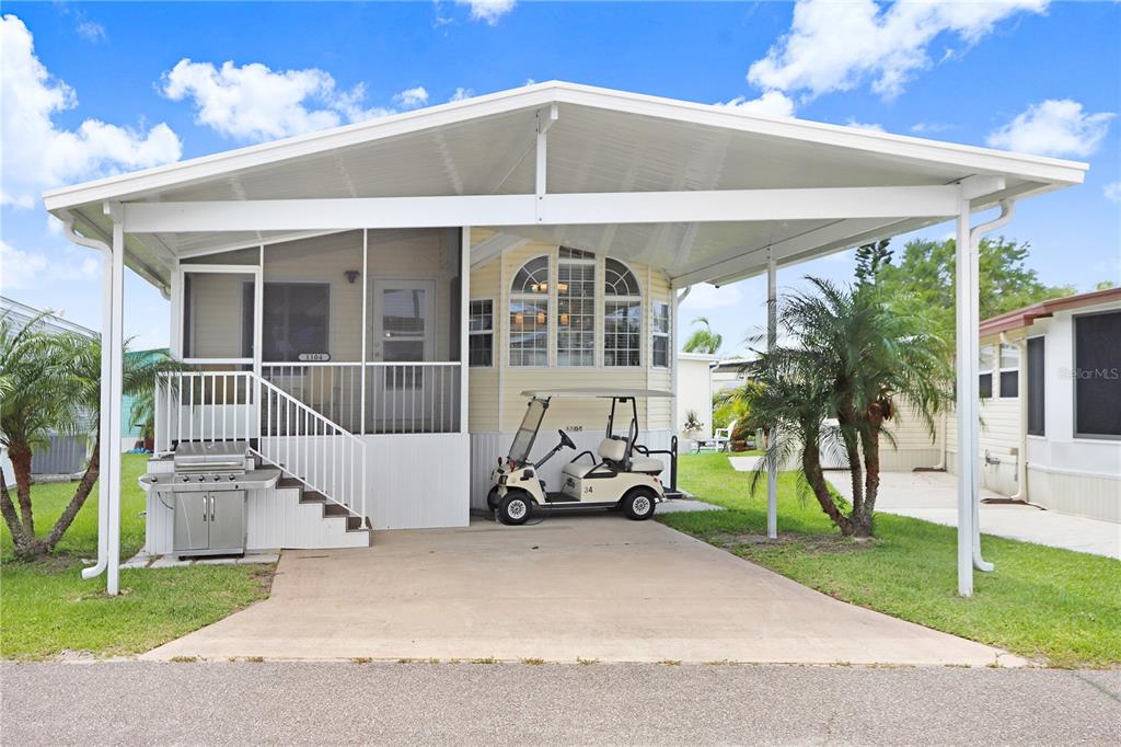 A light yellow manufactured home with a screened porch, carport, and golf cart parked outside — 3333 26TH AVENUE E UNIT 1104, BRADENTON, FL
