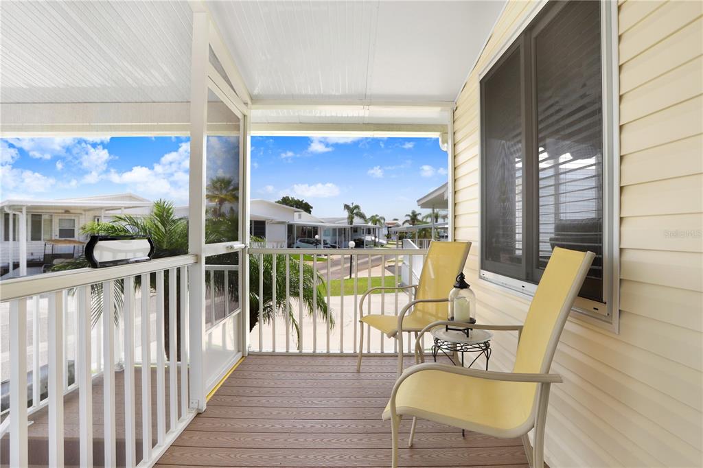 A screened-in porch features light-colored siding, a wood-look floor, and two yellow patio chairs — 3333 26TH AVENUE E UNIT 1104, BRADENTON, FL