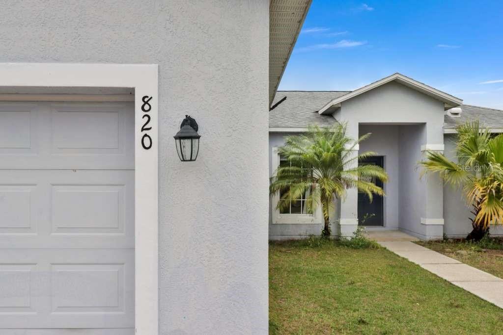 The exterior of a house features a garage with the number 820, a palm tree, and a walkway — 820 GRANTHAM DRIVE, KISSIMMEE, FL