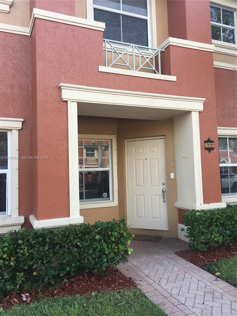 The exterior of a two-story stucco building features a white front door and balcony railing — 11528 NW 60th Ter # 477, Doral FL 33178, DORAL, FL