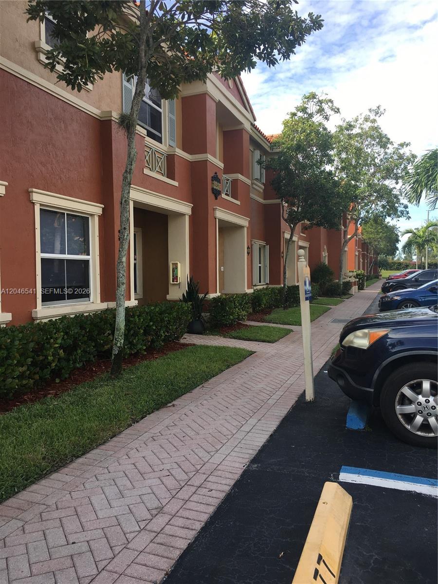 A row of multi-story townhomes with red stucco walls and a paved walkway — 11528 NW 60th Ter # 477, Doral FL 33178, DORAL, FL