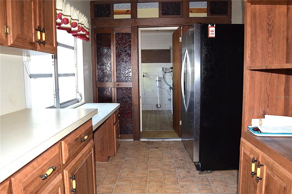 A kitchen with wood cabinets, a black refrigerator, and a doorway leading to a utility area — 2535 BOSWELL STREET, DELTONA, FL