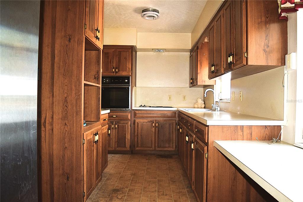 A galley kitchen features wood cabinets, laminate countertops, a built-in oven, and tile flooring — 2535 BOSWELL STREET, DELTONA, FL