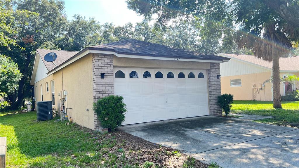 A tan house with a brick-trimmed garage and a white door with arched windows — 1547 OAK HILL TRAIL, KISSIMMEE, FL