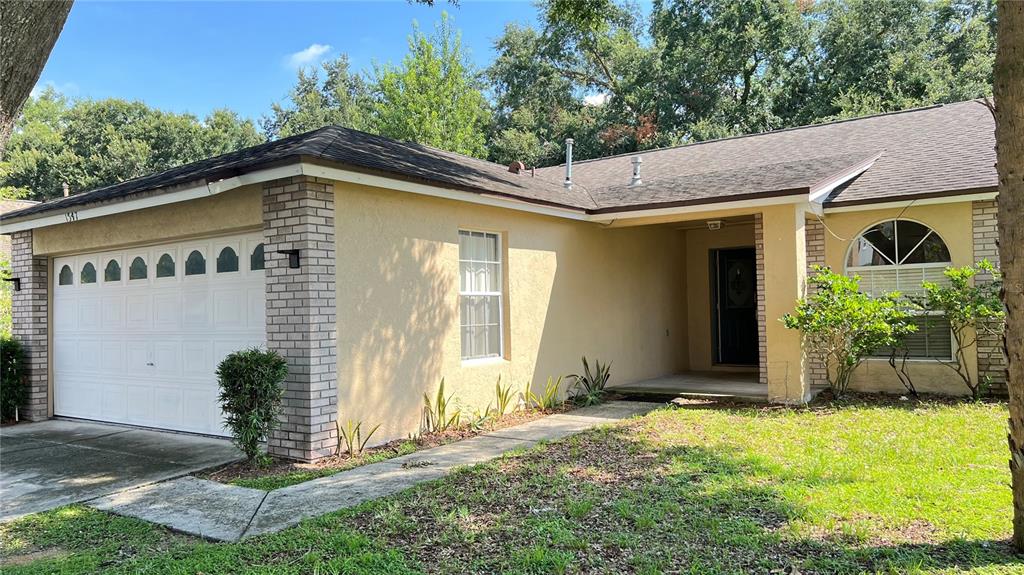 A single-story house with a tan stucco exterior, brick accents, and a two-car garage — 1547 OAK HILL TRAIL, KISSIMMEE, FL