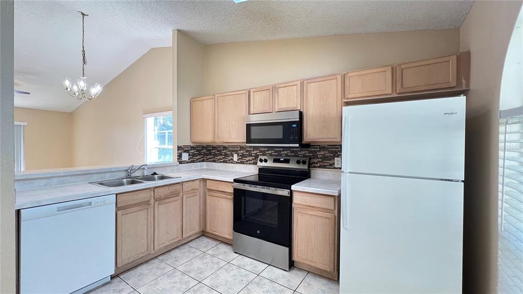 A kitchen features light wood cabinets, stainless steel appliances, and a white dishwasher — 1547 OAK HILL TRAIL, KISSIMMEE, FL