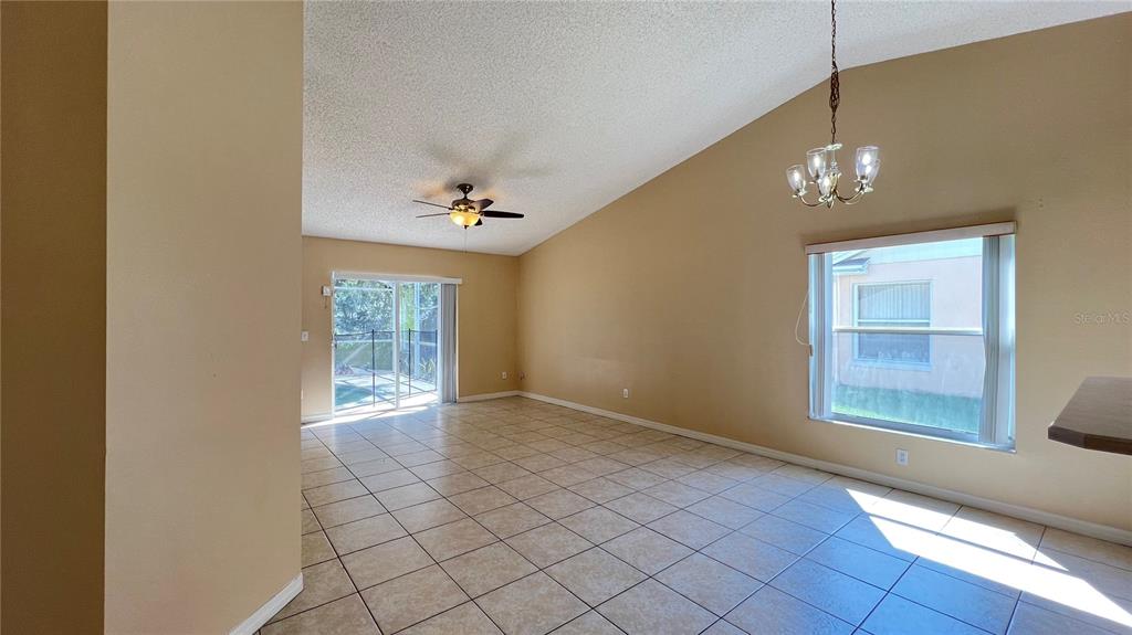 An open living area features vaulted ceilings, tile flooring, a ceiling fan, and sliding doors — 1547 OAK HILL TRAIL, KISSIMMEE, FL