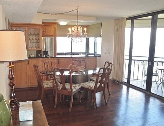 A dining area with a glass table, wooden chairs, and a chandelier near a balcony — 5729 PUERTA DEL SOL BOULEVARD S UNIT 485, ST PETERSBURG, FL