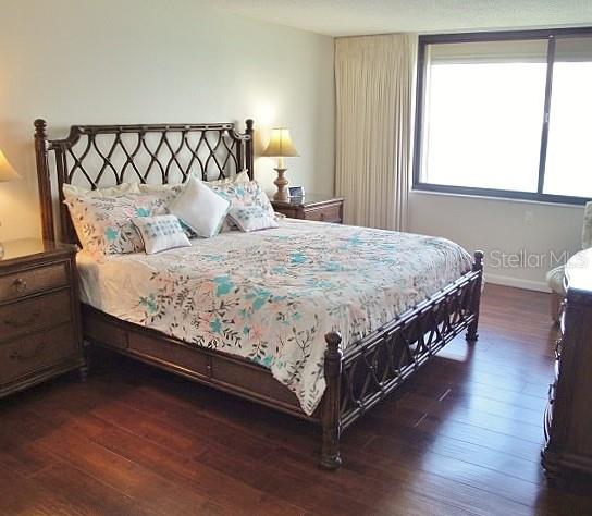 A bedroom features a wooden bed frame, floral bedding, two nightstands, and dark wood flooring — 5729 PUERTA DEL SOL BOULEVARD S UNIT 485, ST PETERSBURG, FL