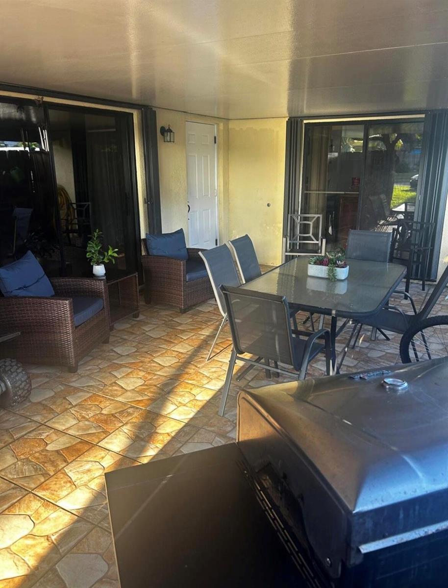 A covered patio features tiled flooring, outdoor furniture, a dining set, and sliding glass doors — 341 Lake Arbor Drive, Palm Springs FL 33461, PALM SPRINGS, FL