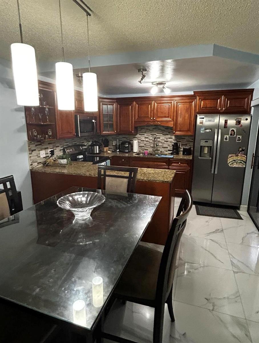A kitchen with wood cabinets, granite countertops, stainless steel appliances, and a dining table — 341 Lake Arbor Drive, Palm Springs FL 33461, PALM SPRINGS, FL