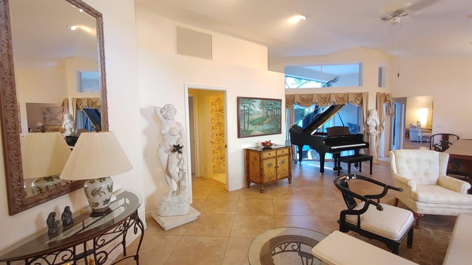A spacious living area features tile flooring, a grand piano, a statue, and a large mirror — 16461 Riverwind Drive, Jupiter FL 33477, JUPITER, FL