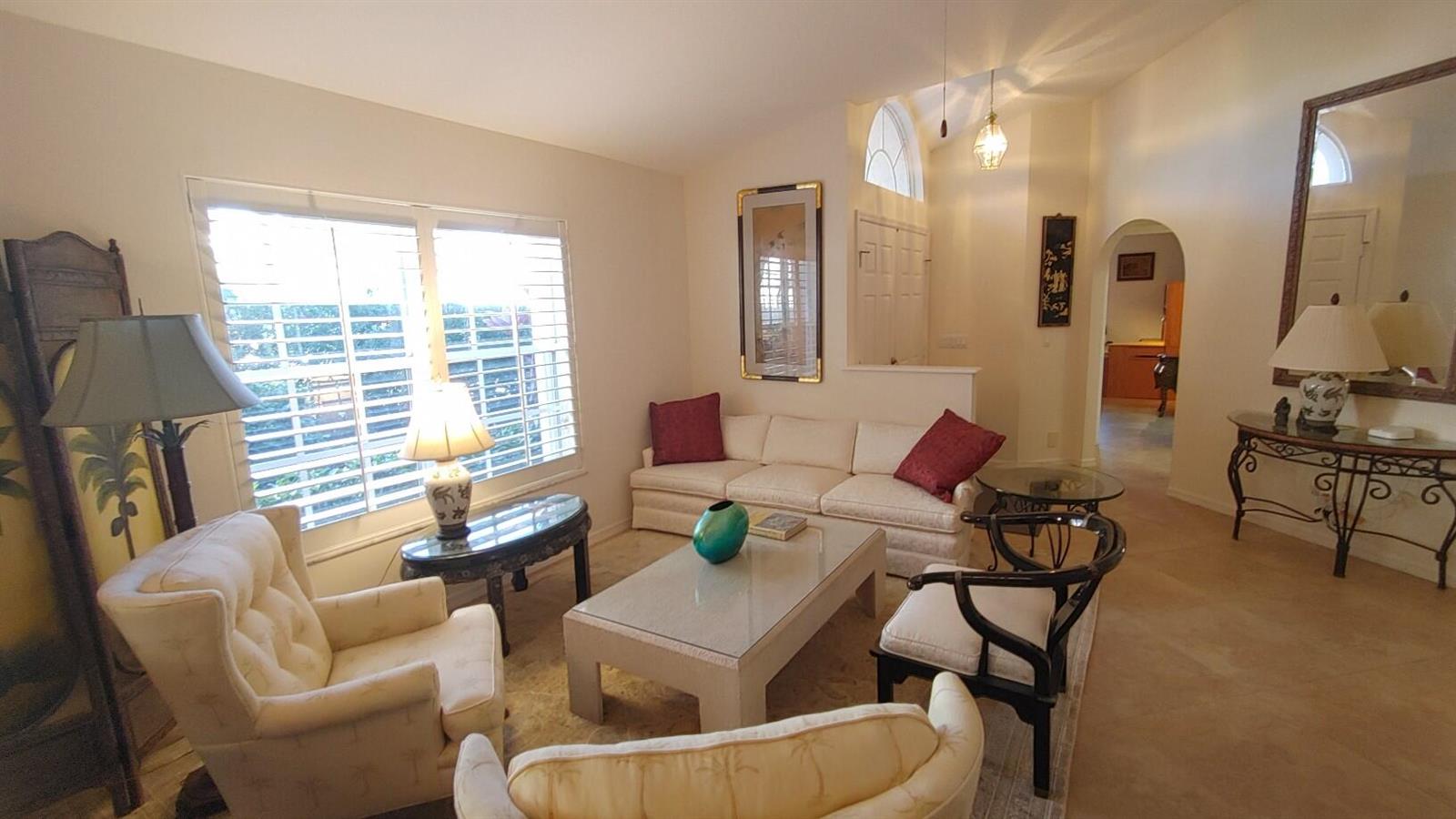 A living room features a white sofa, two armchairs, a glass coffee table, and shutters — 16461 Riverwind Drive, Jupiter FL 33477, JUPITER, FL