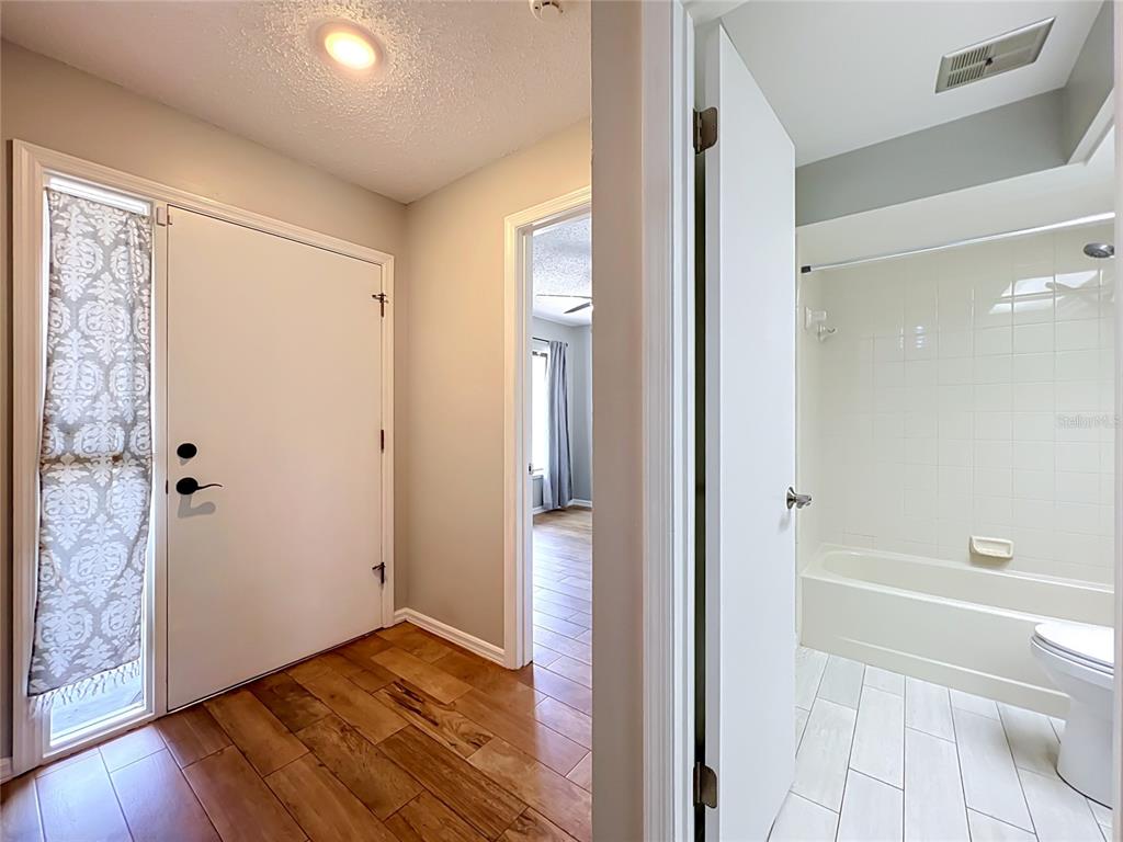 An entryway with wood flooring leads to a bathroom and a room with gray curtains — 2305 SUN VALLEY CIR, WINTER PARK, FL 32792, WINTER PARK, FL