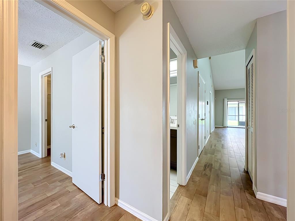 A hallway with light wood-look flooring leads toward a living area with a sliding door — 2305 SUN VALLEY CIR, WINTER PARK, FL 32792, WINTER PARK, FL