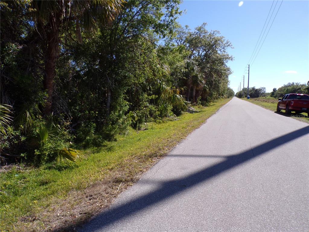 A paved road runs alongside a wooded area with a red truck parked nearby — 26046 SCHAM ROAD, PUNTA GORDA, FL