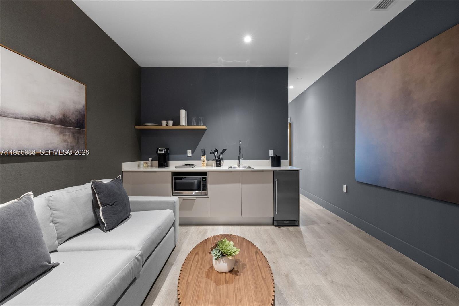A modern kitchenette with light cabinetry and a gray accent wall sits behind a sofa — 229 SW 9th St # 705, Miami FL 33130, MIAMI, FL