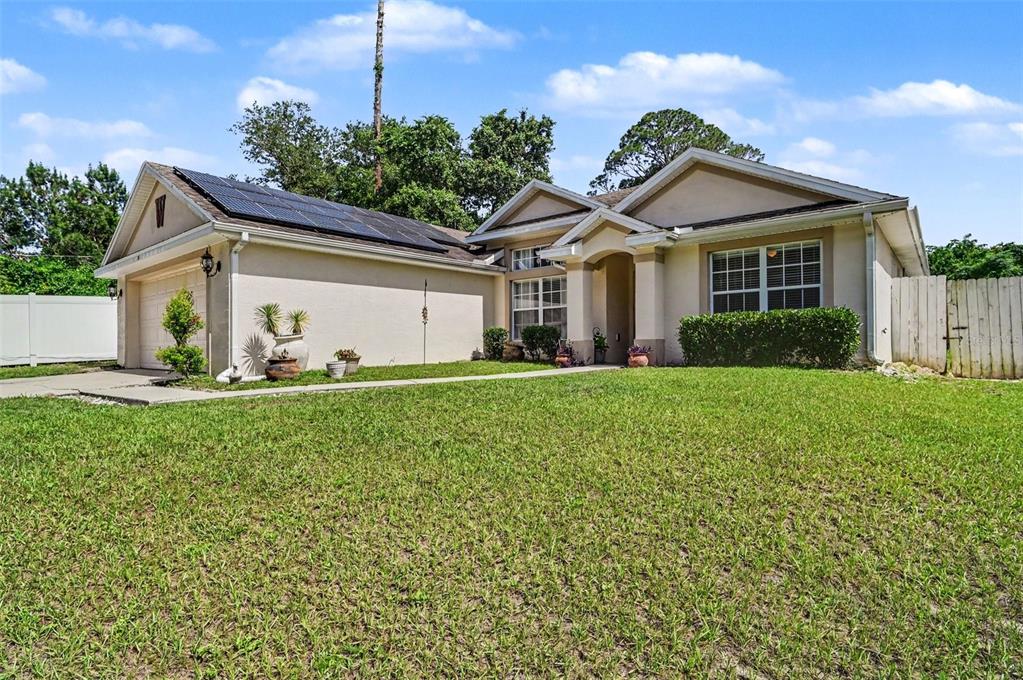 A single-story house with a tan stucco exterior, solar panels on the roof, and lawn — 35 PLANTATION ROAD, DEBARY, FL