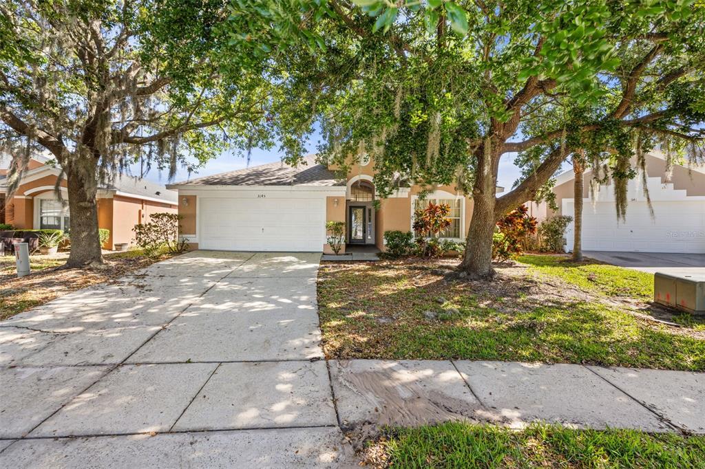 A single-story suburban house with a concrete driveway and large oak trees in the yard — 3145 STONEHURST CIRCLE, KISSIMMEE, FL
