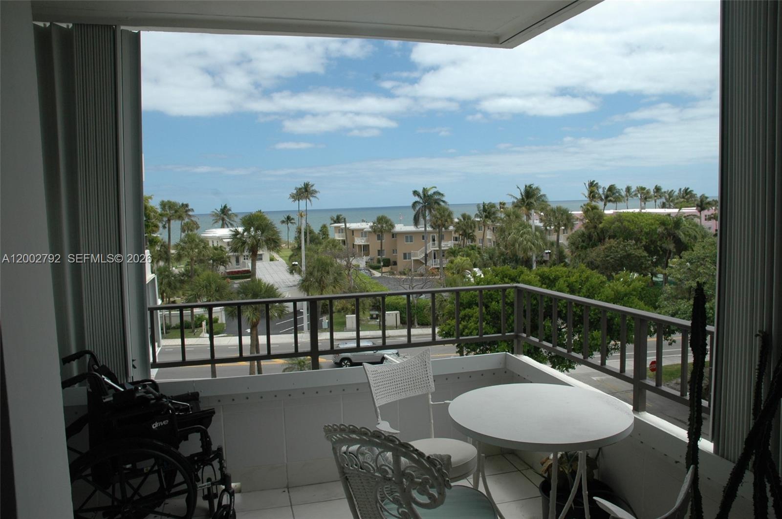A balcony with a table, chairs, and a wheelchair overlooks a street and the ocean — 1401 S Ocean Blvd # 408, Pompano Beach FL 33062, POMPANO BEACH, FL