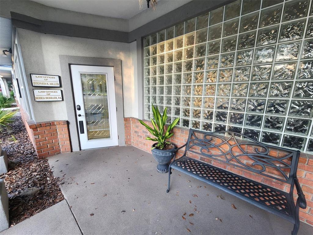 An exterior entrance features a glass-block wall, a metal bench, and signs for law offices — 101 NW 75TH STREET UNIT Suite 1, GAINESVILLE, FL