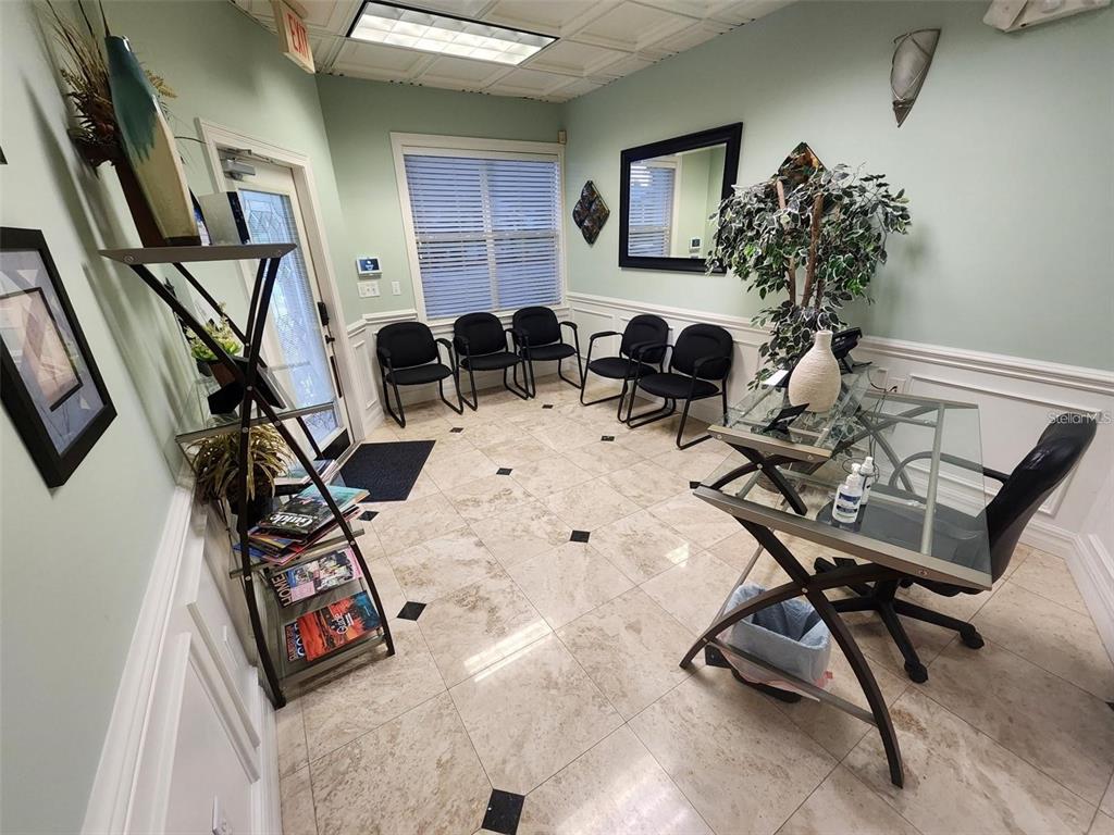 A waiting room features light green walls, a glass desk, black chairs, and tile flooring — 101 NW 75TH STREET UNIT Suite 1, GAINESVILLE, FL