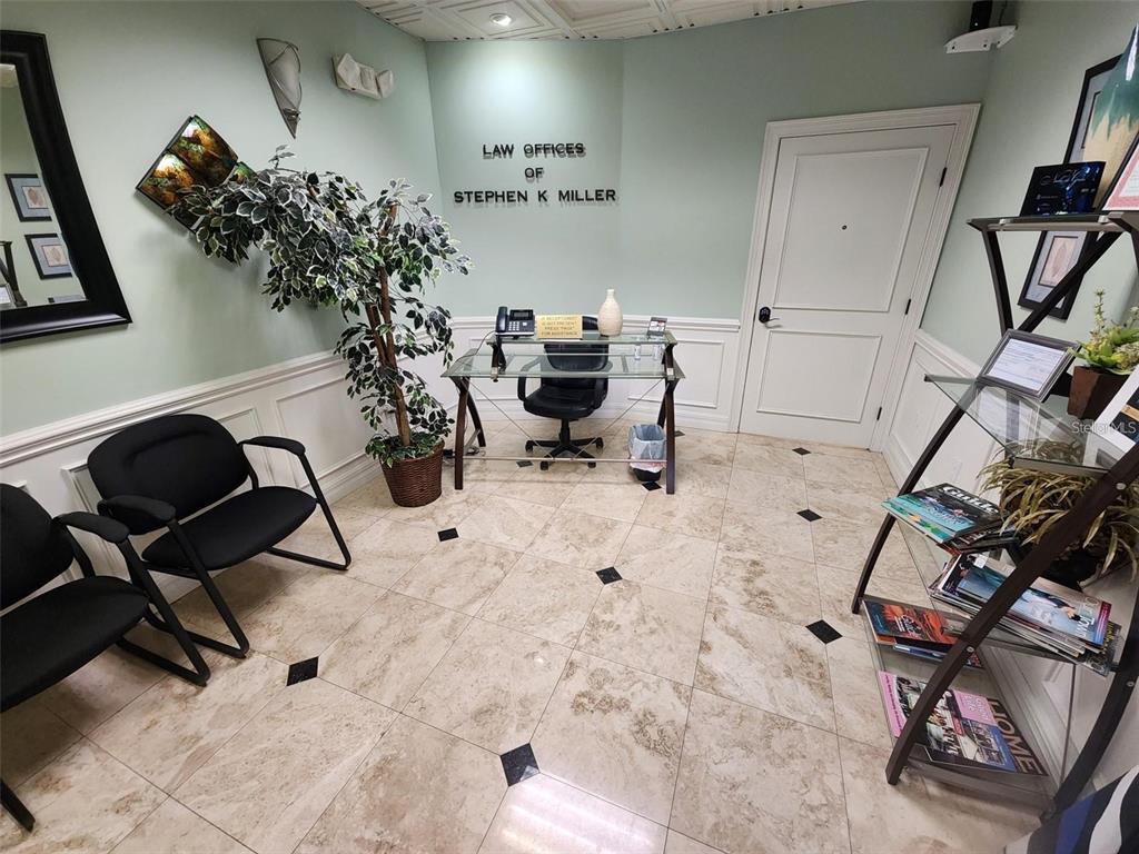 A professional office reception area features tile flooring, a glass desk, and two black chairs — 101 NW 75TH STREET UNIT Suite 1, GAINESVILLE, FL