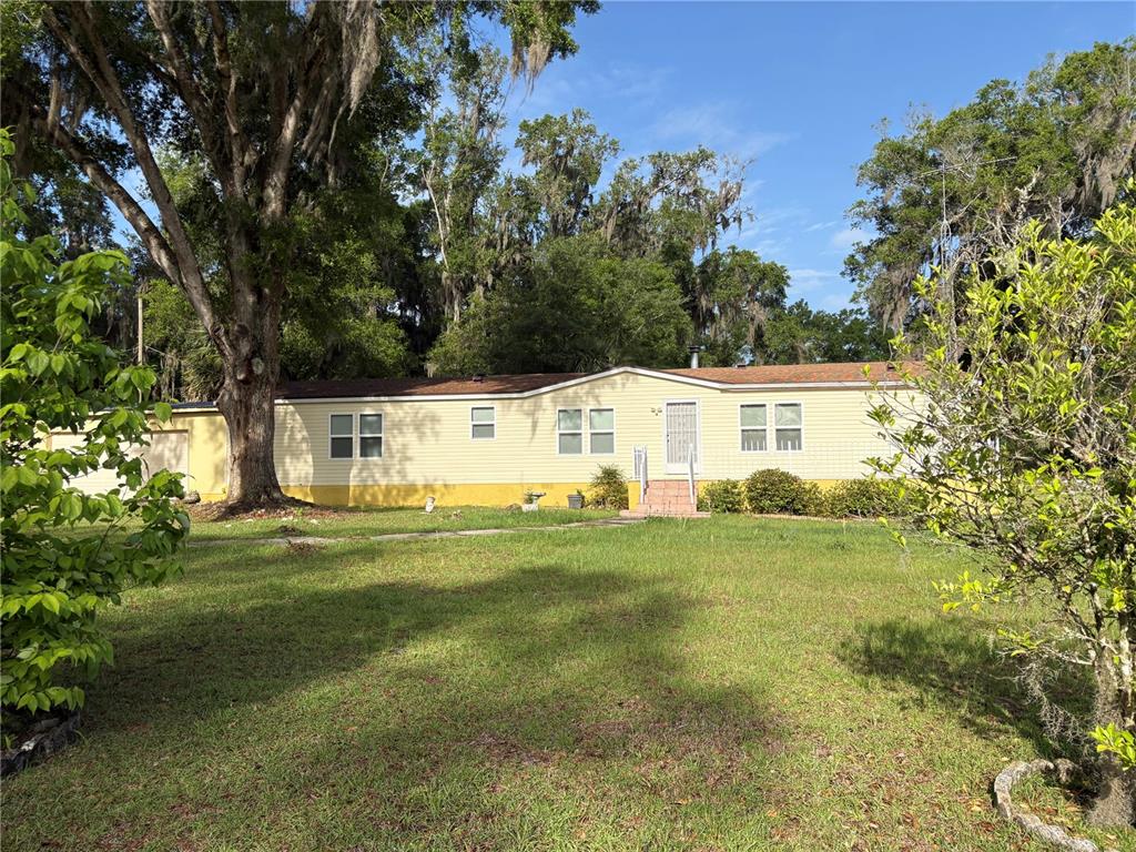 A single-story yellow manufactured home sits on a grassy lot with large oak trees — 14490 SE 80TH AVENUE, SUMMERFIELD, FL