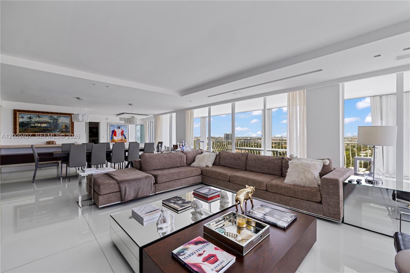 A modern living room features a large brown sectional, mirrored coffee table, and floor-to-ceiling windows — 10155 Collins Ave # 1210, Bal Harbour FL 33154, BAL HARBOUR, FL