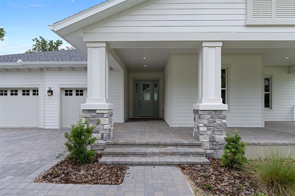 The exterior of a white house features a stone-based porch, columns, and a paved driveway — 4538 MAJESTIC HILLS LOOP, BROOKSVILLE, FL