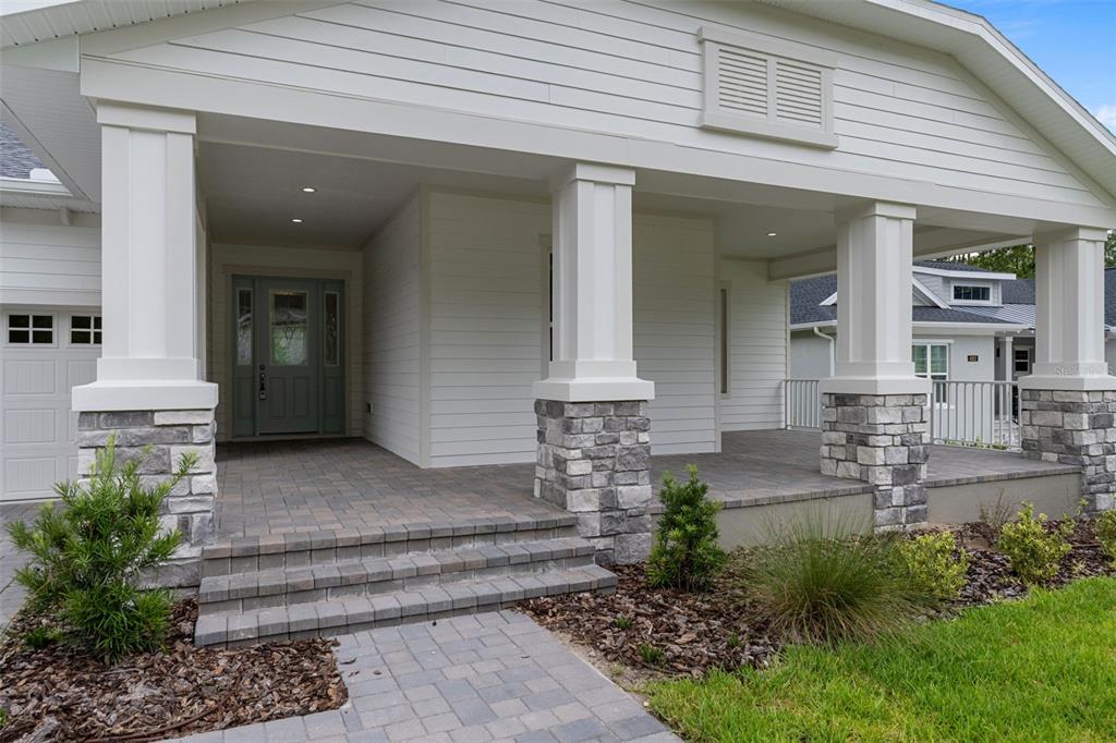 A white house exterior features a covered front porch with stone pillars and paver steps — 4538 MAJESTIC HILLS LOOP, BROOKSVILLE, FL
