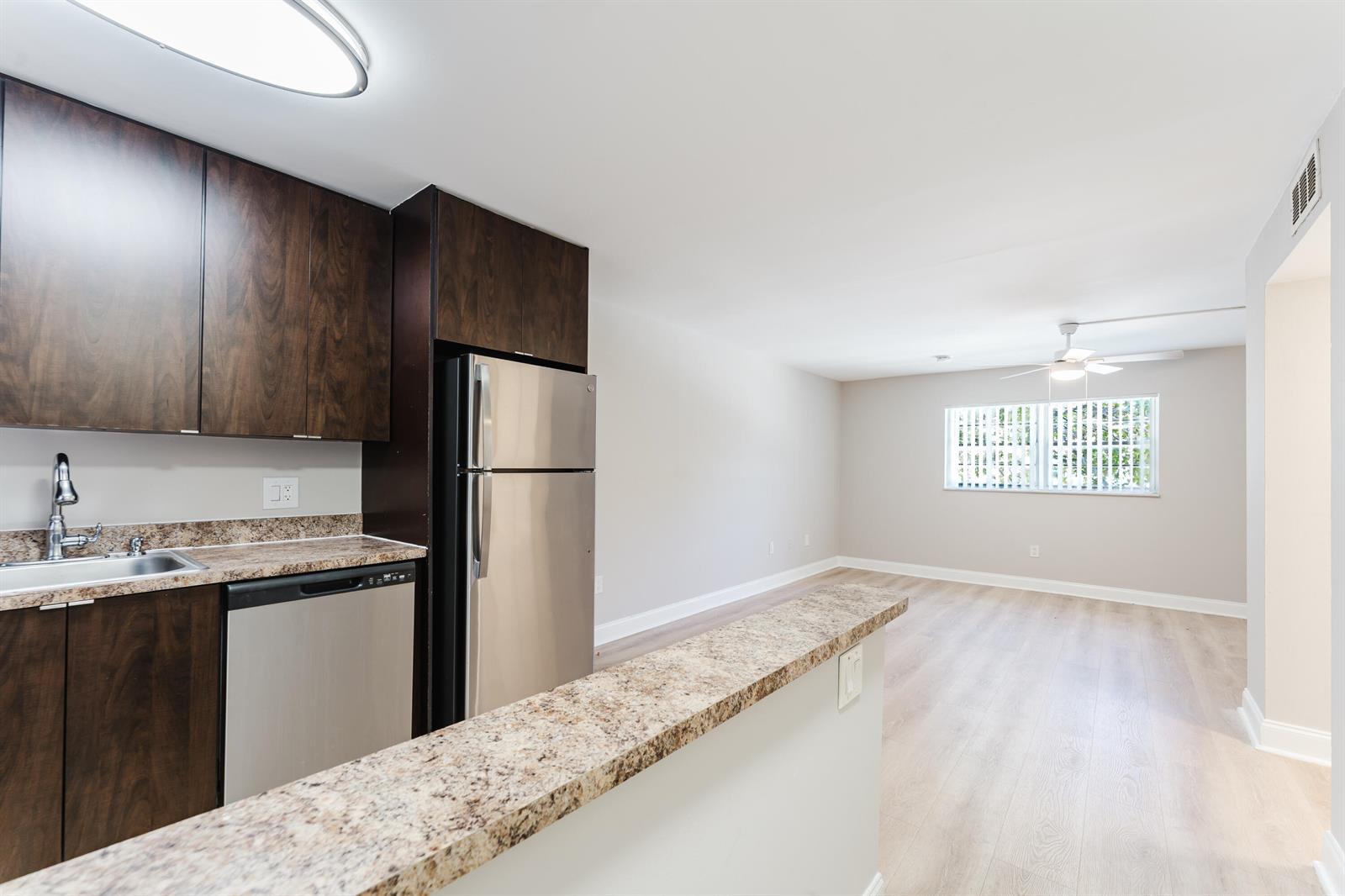 A kitchen with dark wood cabinets and stainless steel appliances overlooks an open living area — 650 SW 2nd Avenue # 252, Boca Raton FL 33432, BOCA RATON, FL
