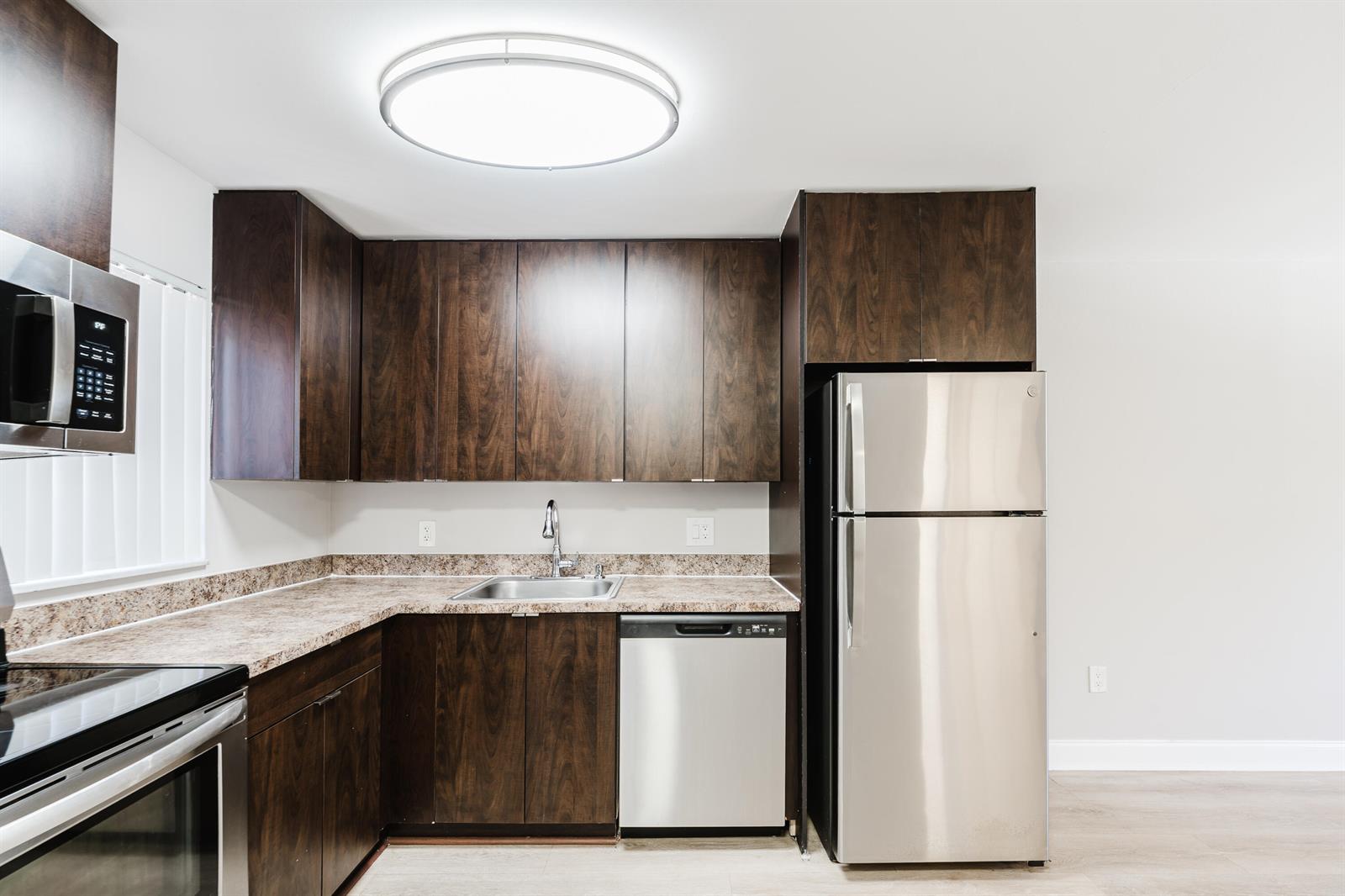 A kitchen features dark wood cabinets, stainless steel appliances, and speckled laminate countertops — 650 SW 2nd Avenue # 252, Boca Raton FL 33432, BOCA RATON, FL