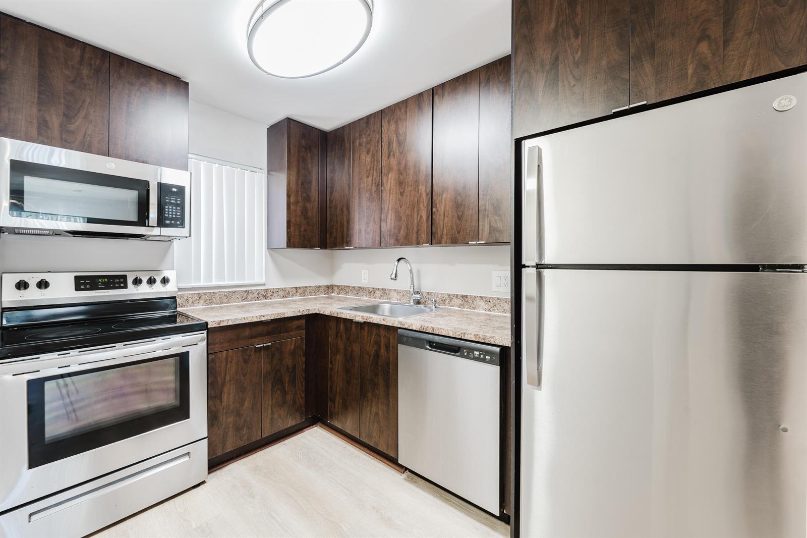 A kitchen features dark wood cabinets, stainless steel appliances, and speckled laminate countertops — 650 SW 2nd Avenue # 252, Boca Raton FL 33432, BOCA RATON, FL