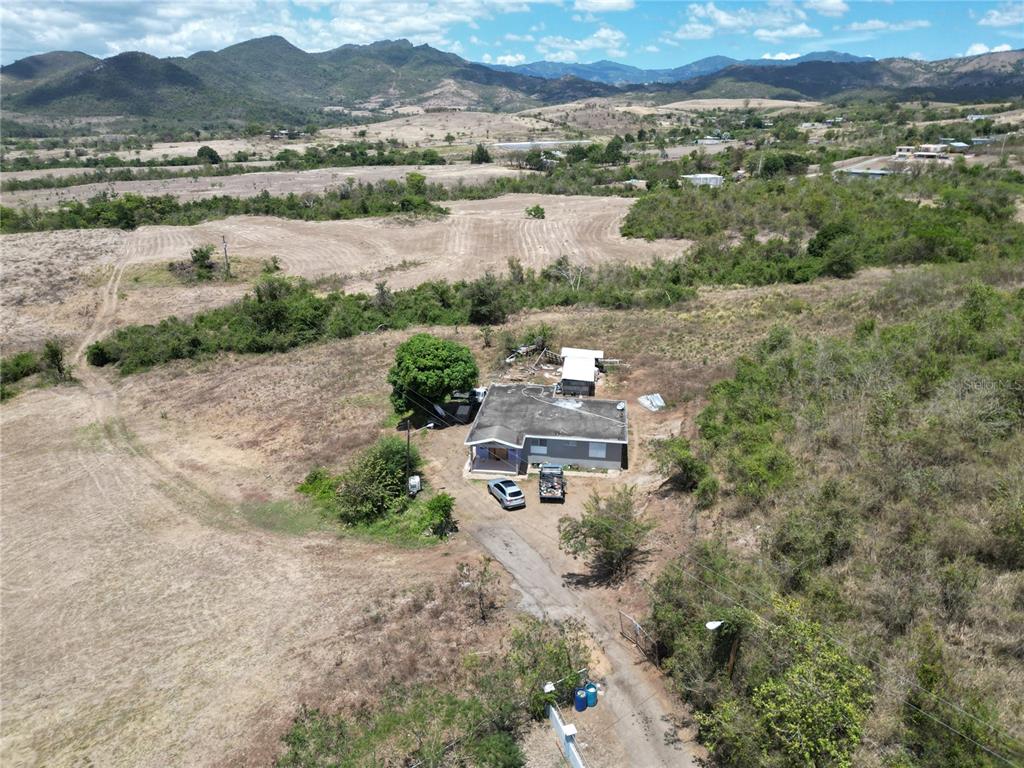 An aerial view shows a single-story house with a driveway surrounded by dry, hilly terrain — 14 LOS LLANOS WARD, COAMO, PR
