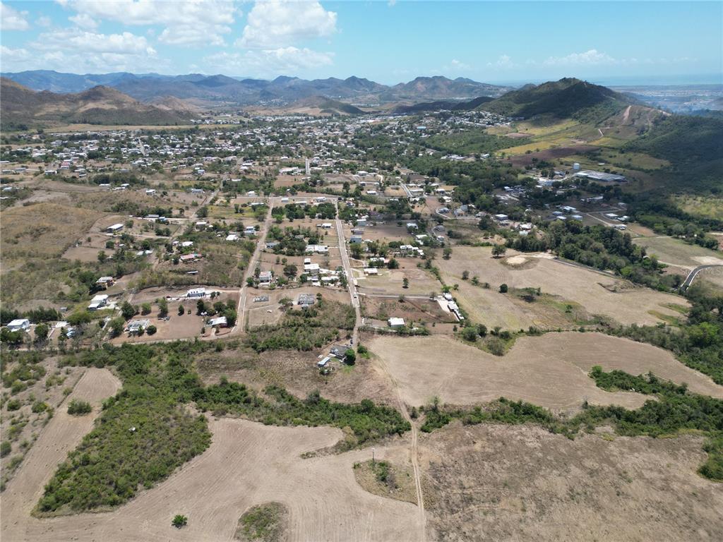 An aerial view shows a rural town nestled among rolling hills and open fields — 14 LOS LLANOS WARD, COAMO, PR