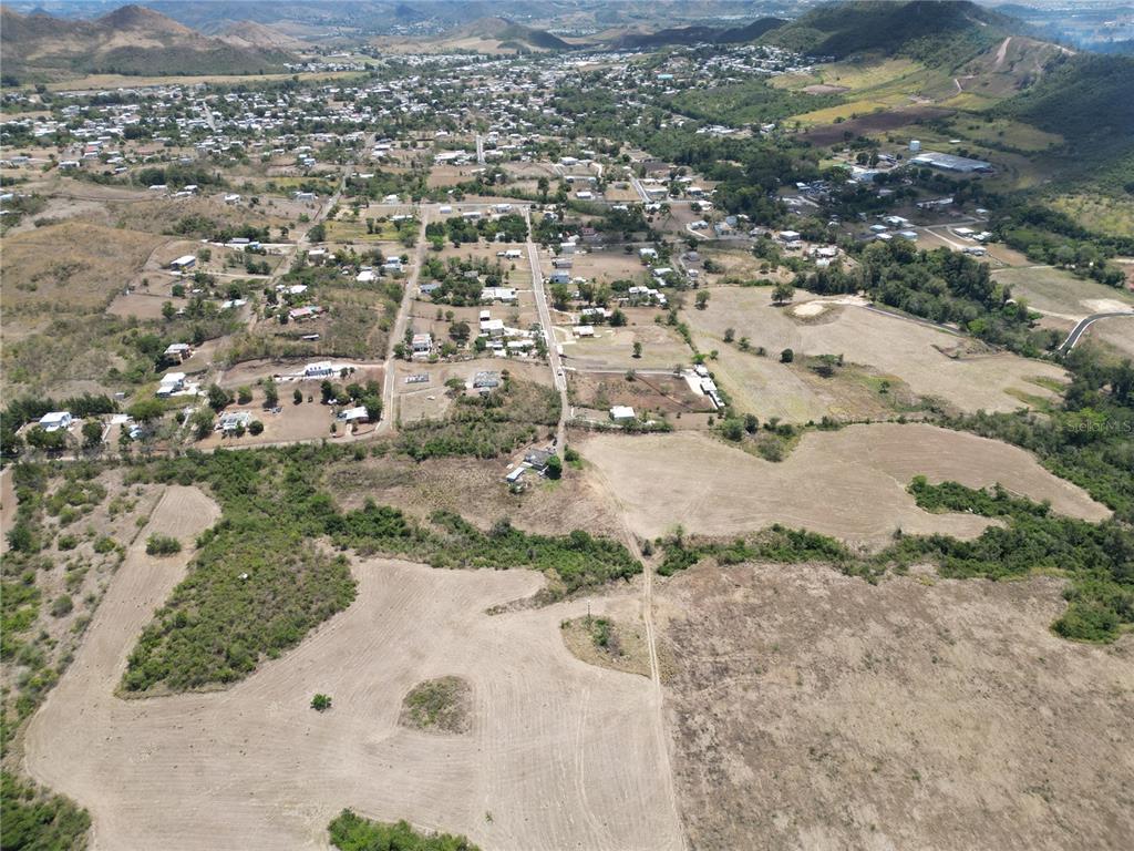 An aerial view shows a rural landscape with scattered houses, dirt roads, and open fields — 14 LOS LLANOS WARD, COAMO, PR