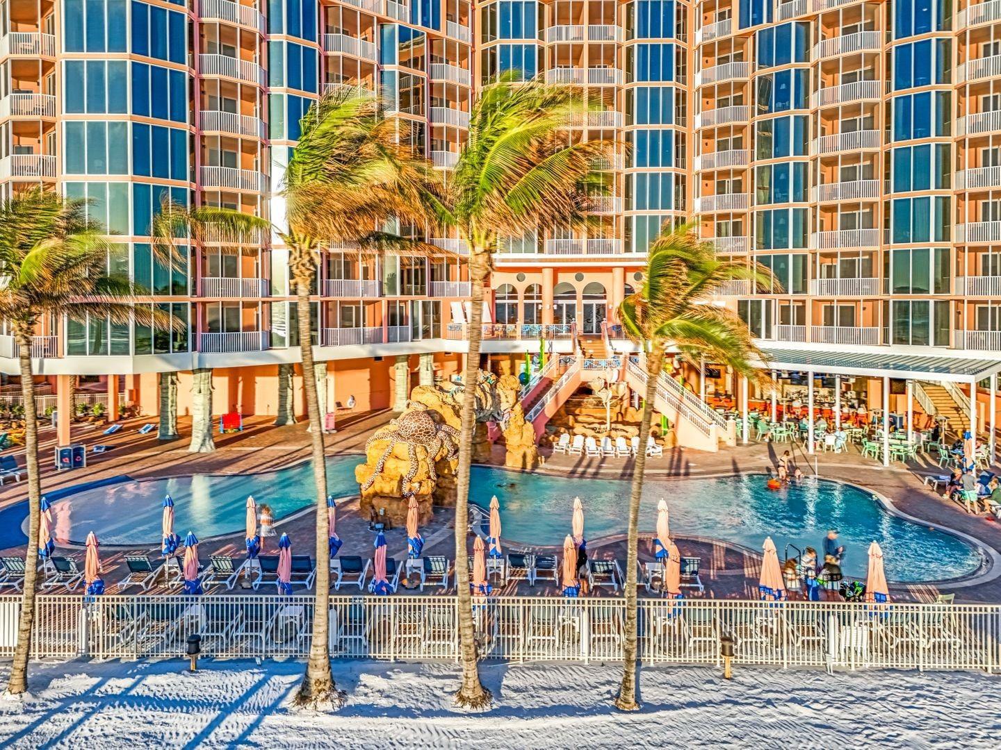 An exterior view of a multi-story resort building featuring a swimming pool and palm trees — 200 Estero Boulevard # 207, FL 33931, FL