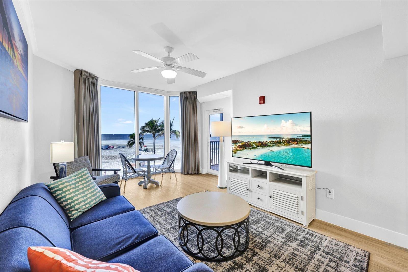 A living room with a blue sofa, a round coffee table, and floor-to-ceiling beach views — 200 Estero Boulevard # 207, FL 33931, FL
