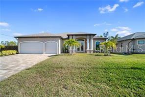 A single-story house with a beige stucco exterior, a multi-car garage, and palm trees — 2341 NW 36TH PLACE, CAPE CORAL, FL