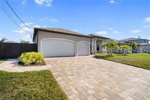 A two-car garage with open doors, storage shelving, and a paved driveway — 2341 NW 36TH PLACE, CAPE CORAL, FL