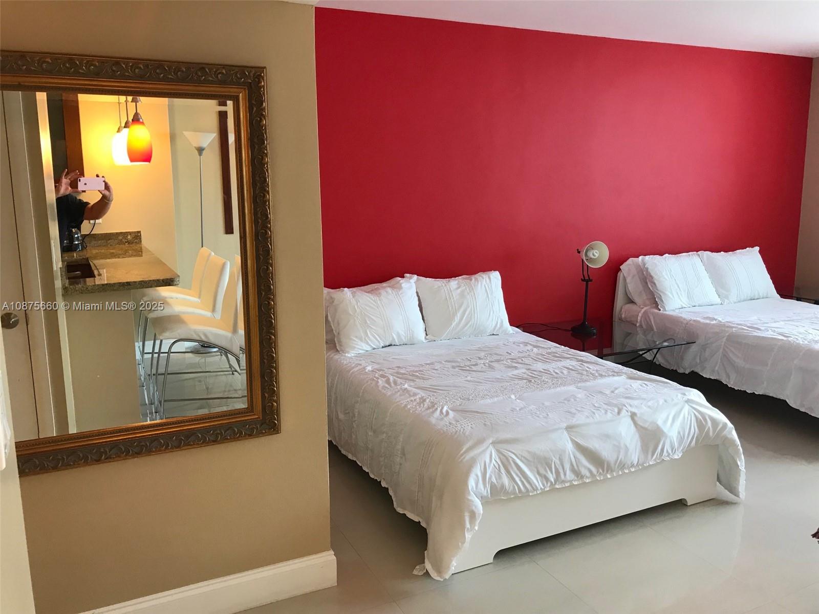 A bedroom with two beds, a red accent wall, and a large ornate mirror — 100 Lincoln Rd # 1226, Miami Beach FL 33139, MIAMI BEACH, FL