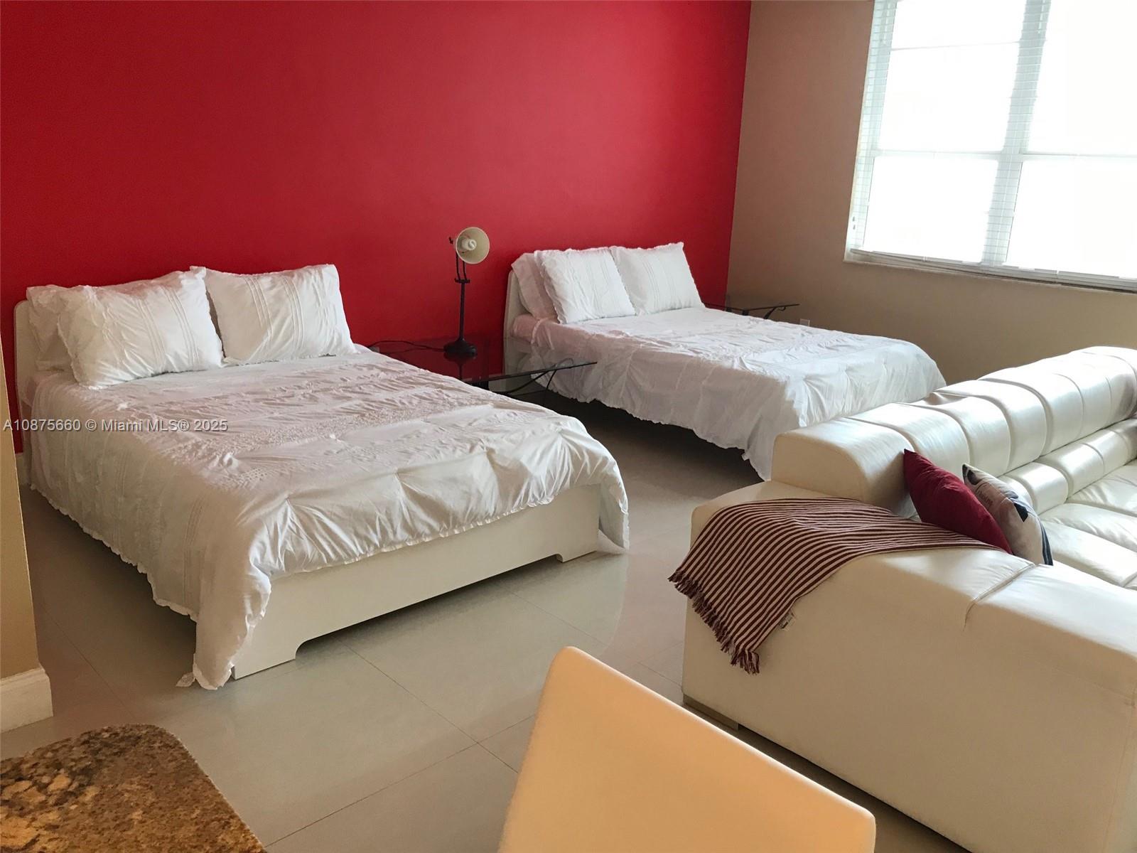 A bedroom features two white beds, a white leather sofa, and a red accent wall — 100 Lincoln Rd # 1226, Miami Beach FL 33139, MIAMI BEACH, FL