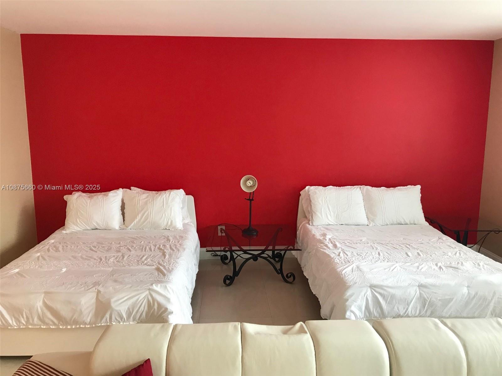 A bedroom features two beds with white bedding against a bright red accent wall — 100 Lincoln Rd # 1226, Miami Beach FL 33139, MIAMI BEACH, FL