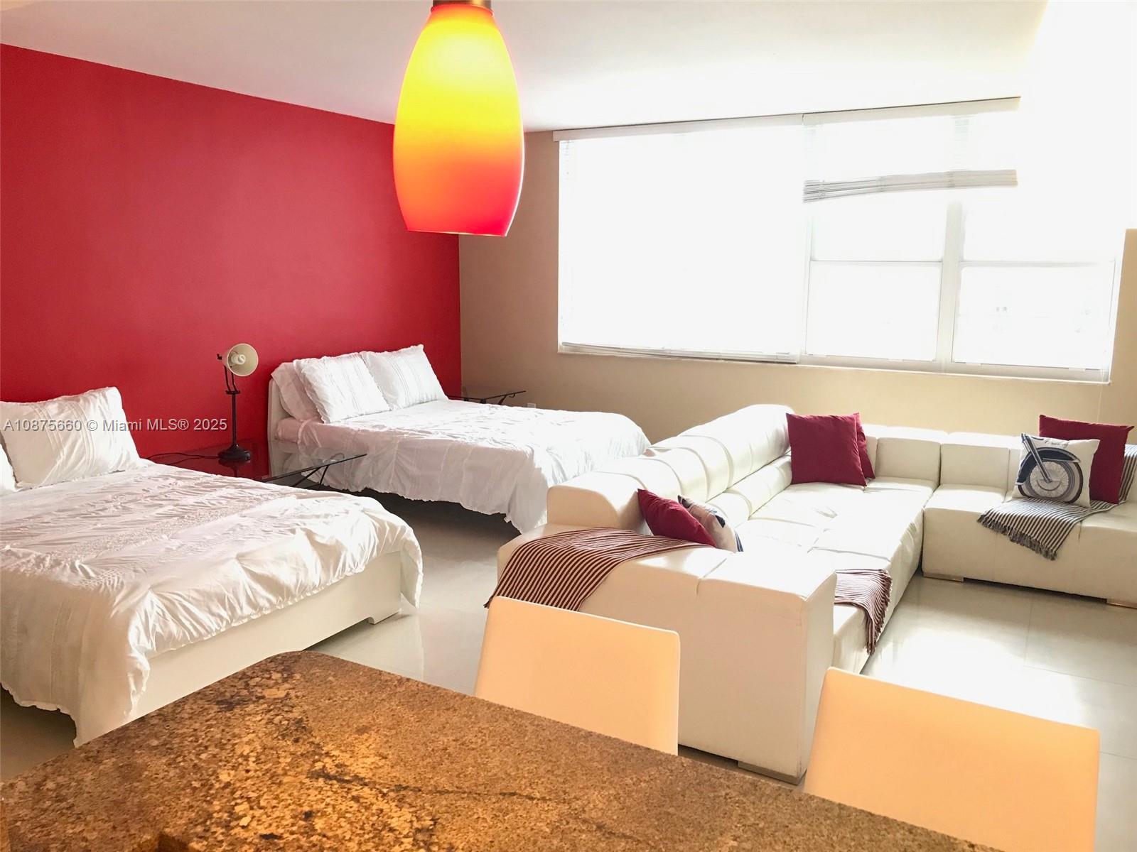 A studio apartment features two beds, a white sectional sofa, and a red accent wall — 100 Lincoln Rd # 1226, Miami Beach FL 33139, MIAMI BEACH, FL